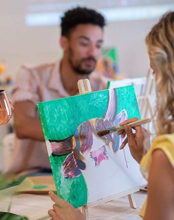 A woman is painting a colourful picture of a Highland Cow, while a man paints in the background