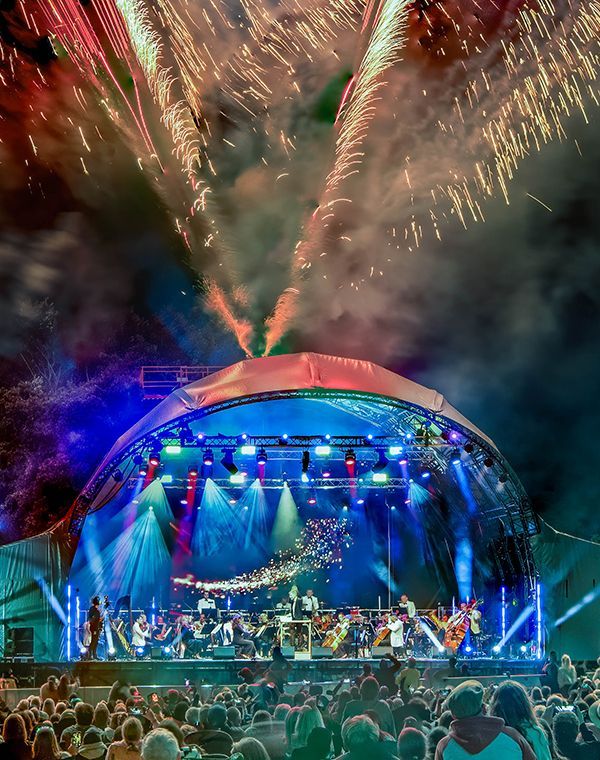 An outdoor stage full of lights under fireworks