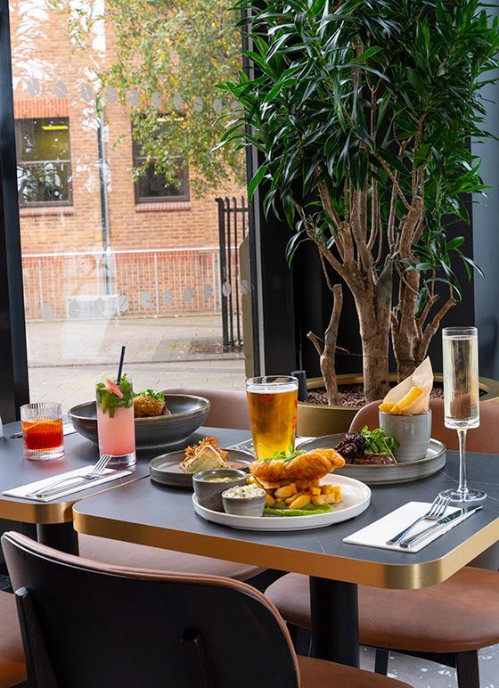 A restaurant table laid out with delicious meals, beers and cocktails